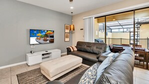 Un salon moderne doté d’un téléviseur à écran plat, de canapés en cuir, d’un meuble de rangement blanc et d’une grande porte-fenêtre coulissante donnant sur un espace extérieur.