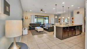 Une cuisine moderne avec un îlot central, un coin repas comprenant un canapé et une table, et un salon avec un divan et une lampe.