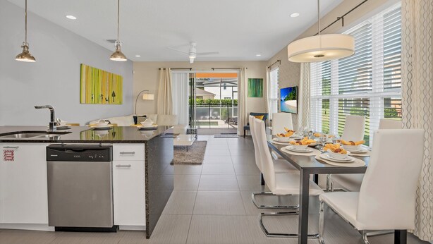 A modern kitchen with a dishwasher, a dining area with a table set for four, and a view of the outdoors through large windows.