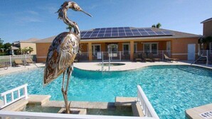A swimming pool with a bird sculpture, a building with solar panels, and a fenced area with lounge chairs.