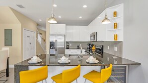 A modern kitchen with white cabinets, a granite countertop, and three yellow bar stools.