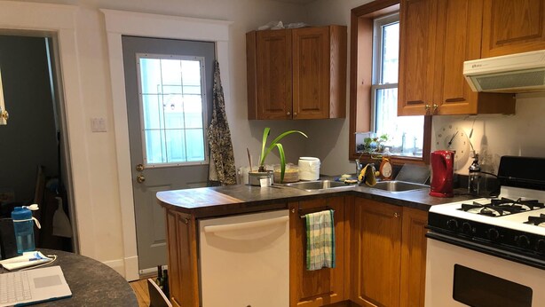 Een keuken met houten kastjes, een fornuis, een spoelbak en een raam.