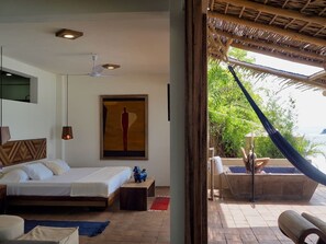 Relax in a serene space with a large bed, bedside table, and wall-mounted artwork, offering a view of lush greenery and the pool area.