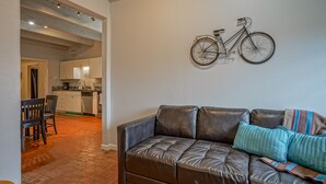 A living room with a brown leather sofa, a teal pillow, and a bicycle mounted on the wall. - #2 in Old Town, 2bd/2ba, near I-40 (Albuquerque)