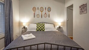 A neatly made bed with a checkered bedspread, two bedside lamps, and a wall-mounted tennis racket display. - #2 in Old Town, 2bd/2ba, near I-40 (Albuquerque)