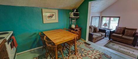 A cozy living room with a wooden dining table, a sofa, and a patterned rug.
