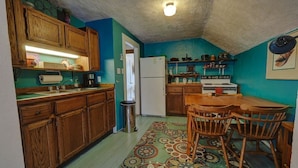 A compact kitchen with wooden cabinets, a refrigerator, a stove, and a dining table with chairs. - Upper Level Loft in Downtown Suttons Bay Across the Street From Beach and Marina (Suttons Bay)