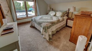 A bedroom with a bed, bedside table, lamp, and a window with a view of a street. - Upper Level Loft in Downtown Suttons Bay Across the Street From Beach and Marina (Suttons Bay)
