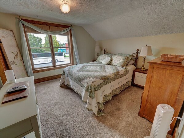 A bedroom with a bed, bedside table, lamp, and a window with a view of a street. - Upper Level Loft in Downtown Suttons Bay Across the Street From Beach and Marina (Suttons Bay)