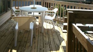 A wooden deck with a table and chairs, an umbrella, and a view of a house and trees. - Upper Level Loft in Downtown Suttons Bay Across the Street From Beach and Marina (Suttons Bay)