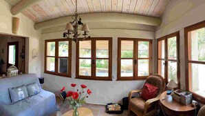 A cozy room with a curved ceiling, wooden beams, a blue sofa, a wicker chair, and large windows offering a view of greenery. - Pretty Mas provençal, private pool, Airco, 5bed (10p), 3bath, Boulodrome, Hammock. (Saint-Michel-d'Euzet)