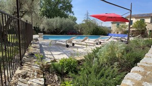 A pool area with lounge chairs, a red umbrella, and a stone wall. - Pretty Mas provençal, private pool, Airco, 5bed (10p), 3bath, Boulodrome, Hammock. (Saint-Michel-d'Euzet)