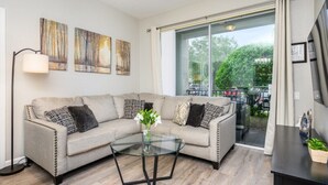 A modern living room with a beige sofa, a glass coffee table, and artwork on the wall. - Epic Universe New Listing Beautiful Vacation Condo - 3018 (Orlando)