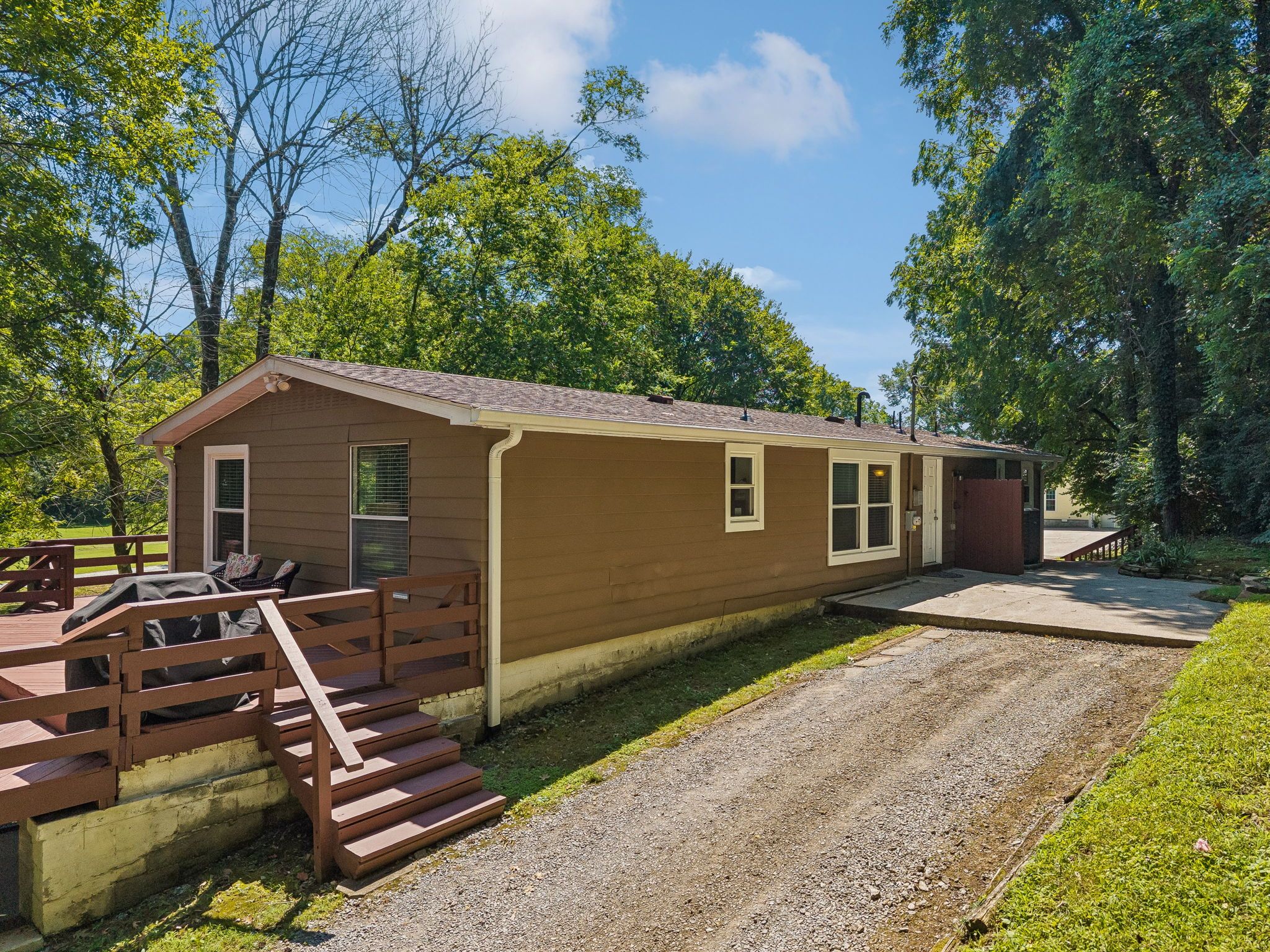 A single-story building with a porch, a covered grill area, and a gravel driveway.