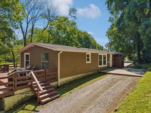 A single-story building with a porch, a covered grill area, and a gravel driveway.