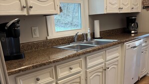 Una cocina con armarios blancos, encimera de granito, cafetera y lavavajillas.