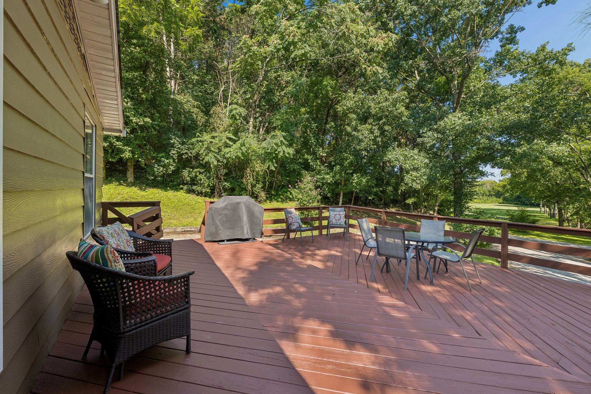 A wooden deck with outdoor furniture, including chairs and a table, overlooking a lush green landscape.
