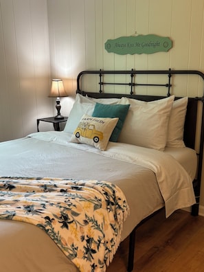 A neatly made bed with a floral blanket, a lamp on a bedside table, and a sign above the bed.