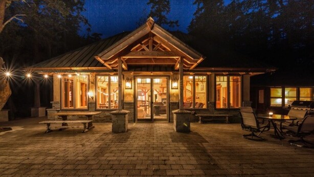 Eine Lodge mit Holzfassade, großen Glasüren und Außenbestuhlung.