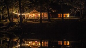 Eine Holzhütte mit Spiegelung im Wasser, umgeben von Bäumen.