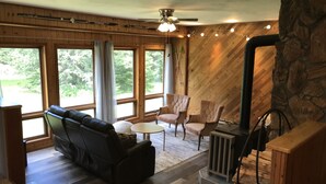 Een gezellige woonkamer met een open haard, een leren bank en twee fauteuils. Grote ramen bieden uitzicht op het landschap.