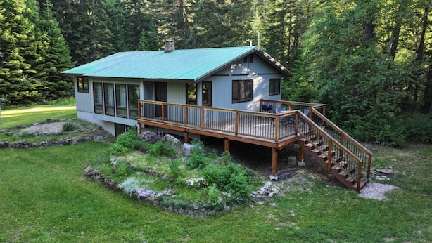 Een chalet met terras en trap, omgeven door een aangelegde tuin en bos.