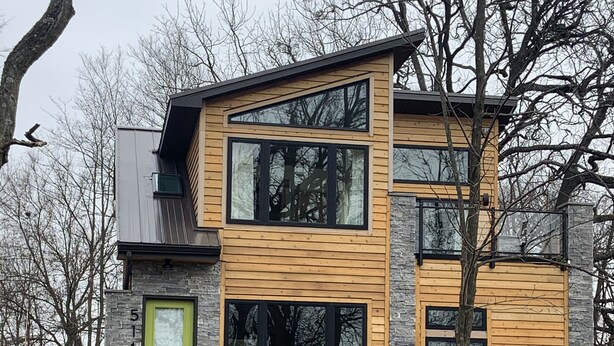 Una casa moderna de dos pisos con fachada de piedra y paneles de madera.