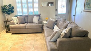 A living room with two grey sofas, a small side table, a potted plant, and a door with a mirror and window. - Retreat w/ Pool  & Spa Home in Palm Desert 
There is a 300.00 fee to heat pool 
 (Palm Desert)