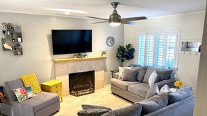 A living room with a fireplace, two sofas, a TV, and a ceiling fan. - Retreat w/ Pool  & Spa Home in Palm Desert 
There is a 300.00 fee to heat pool 
 (Palm Desert)