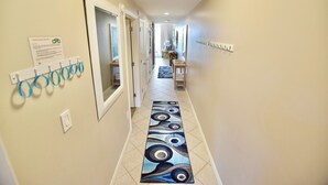 A hallway with a patterned rug, a coat rack, and a door leading to another room. - Destin West Gulfside #309 ~Free Beach Service! Great View! Pools + Lazy River! (Fort Walton Beach)