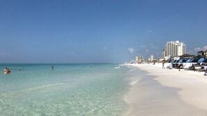 Ein Strand mit klarem türkisblauem Wasser, einem sandigen Ufer und einer Reihe von Strandgebäuden mit Sonnenschirmen.