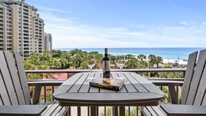 Ein Balkon mit Tisch, zwei Stühlen, einem Buch mit dem Titel 'Dying' und zwei Weingläsern sowie einer Flasche darauf.