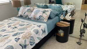 Ein Schlafzimmer mit einem Bett, das mit einem Meeresmotiv-Bettbezug und Kissen ausgestattet ist, zwei Nachttischen mit Lampen und dekorativen Fischskulpturen.
