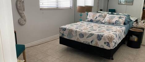 A bedroom with a bed, two windows, a wall decoration, and a lamp.