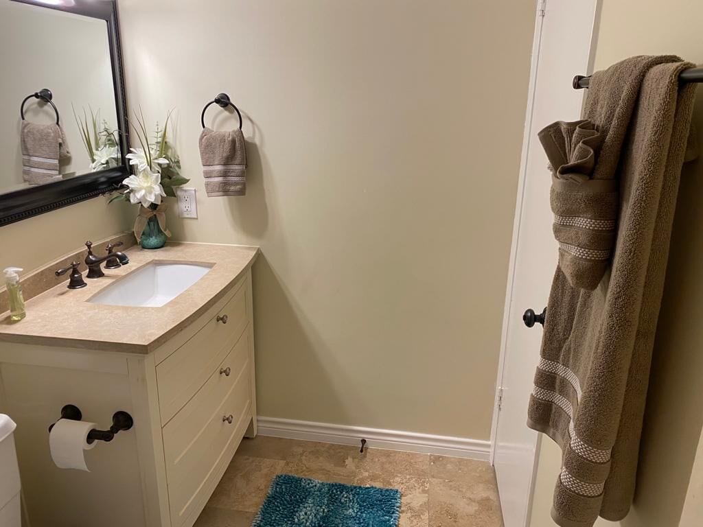 Un baño con un lavabo color beige, un espejo, un perchero con una toalla y una alfombra azul en el suelo.