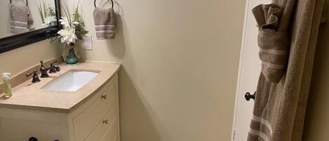 Un baño con un lavabo color beige, un espejo, un perchero con una toalla y una alfombra azul en el suelo.