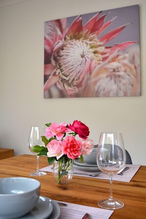 A dining table with a vase of pink flowers, two wine glasses, and a bowl.