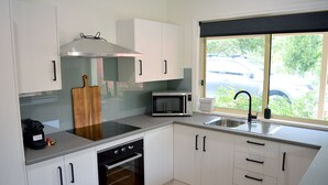 A modern kitchen with white cabinets, a stainless steel range hood, a microwave, a built-in oven, and a window with a view of the outside. - The Blush 1 - Style in the vines (Penwortham)