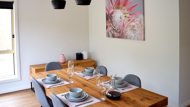 A dining area with a wooden table set for four, featuring grey plates, bowls, and glasses. - The Blush 1 - Style in the vines (Penwortham)