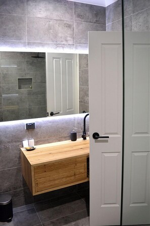 A modern bathroom with a wooden vanity, a mirror, and a white door.