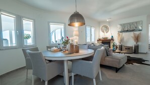 A modern living room with a round dining table, grey chairs, a grey sofa, and a fireplace.