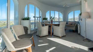 A sunlit room with large windows, wicker furniture, and a table with chairs.