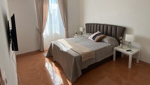 A bedroom with a bed, nightstands, a lamp, a TV, and a window with curtains. - Appartamento Stazione Termini A/C WI FI (Roma)