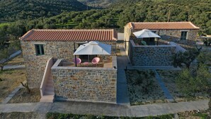 Una villa de piedra con terraza y dos habitaciones, cada una con tejado de baldosas y un pequeño balcón.