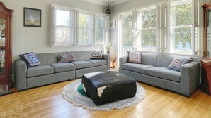 A living room with two grey sofas, a black ottoman, and a wooden floor.