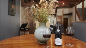 Une table en bois sur laquelle se trouvent un vase de fleurs séchées, une bouteille de vin et deux verres à vin.
