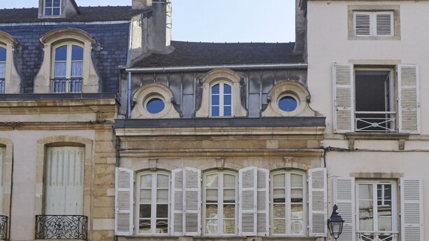Une rangée de bâtiments historiques à l’architecture classique, caractérisés par des fenêtres en arc et des volets traditionnels.