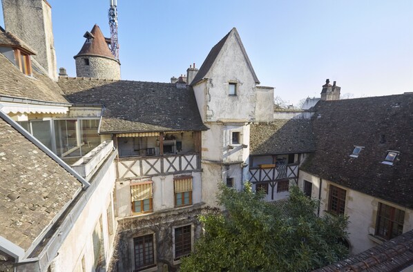 Un pueblo europeo tradicional con una mezcla de edificios de piedra y entramado de madera, incluyendo una torre y un balcón con cerramiento de vidrio.
