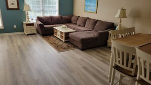 A living room with a sectional sofa, a coffee table, a rug, a dining table with chairs, and a window with blinds. - 🏖️AMAZING 4 Bd, West Ocean City 🏖️ (Ocean City)