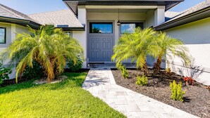 Une maison moderne avec une porte grise, une allée pavée et des palmiers dans le jardin.